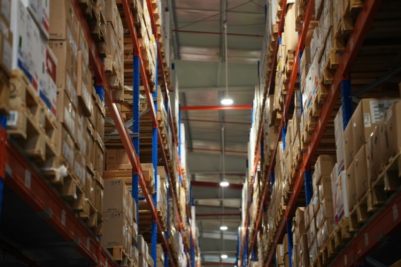 In a factory, photo from the middle of an aisle with stacks of cardboard boxes on either side.